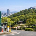 春から初夏の比治山公園。駐車場入口の案内看板が見え、背景に広島市街と緑豊かな公園