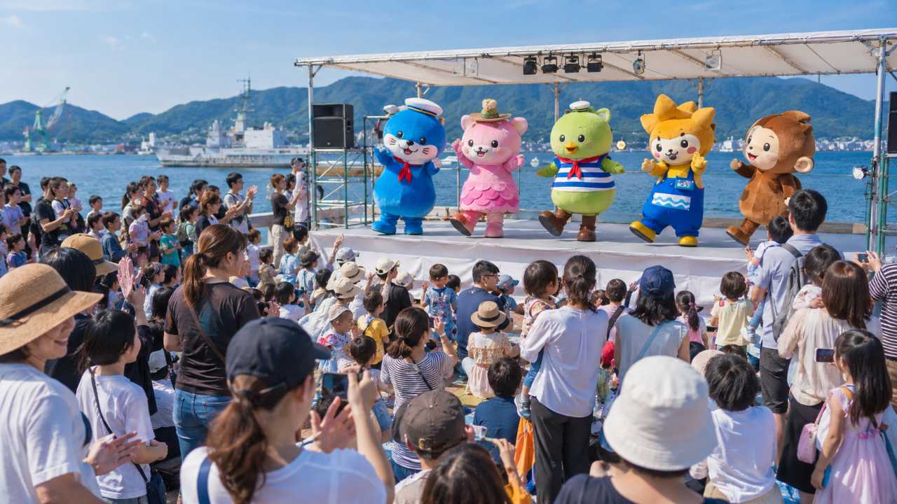呉ご当地キャラ祭のステージイベントを楽しむ観客と、カラフルなキャラクターたちのパフォーマンス風景
