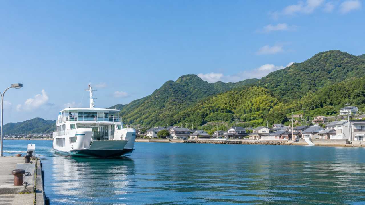似島港に到着するフェリーと小さな港町の風景。穏やかな海、桟橋、島の山並み、旅の始まりを感じる写真風