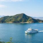 広島湾に浮かぶ似島をテーマにしたブログ用アイキャッチ画像。穏やかな瀬戸内海、緑の山、遠くに広島市街、手前に白いフェリーが進む構図