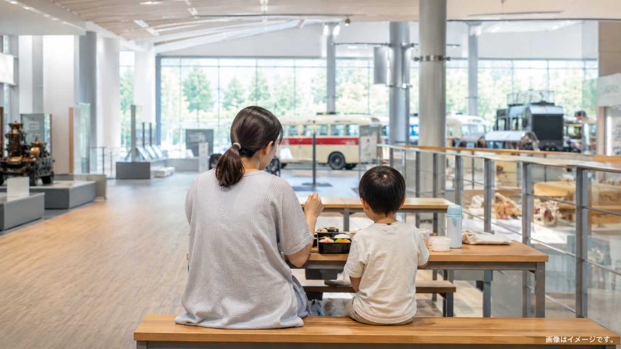 博物館の1階休憩スペースをイメージした明るいベンチと親子のお弁当ランチ、清潔で落ち着いた写真風